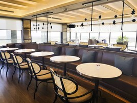 A modern cafe with round tables and cushioned seating, large windows, and hanging pendant lights.