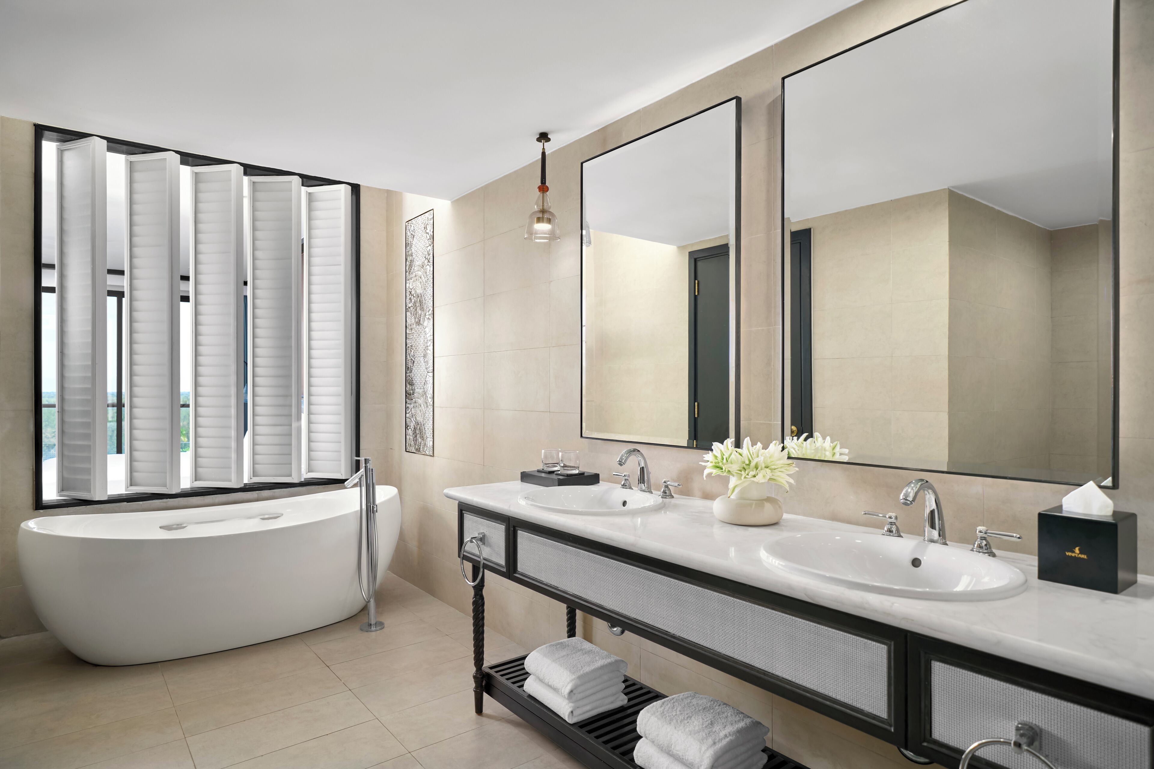 A modern bathroom with a freestanding bathtub, two sinks, a large mirror, and a window with blinds.