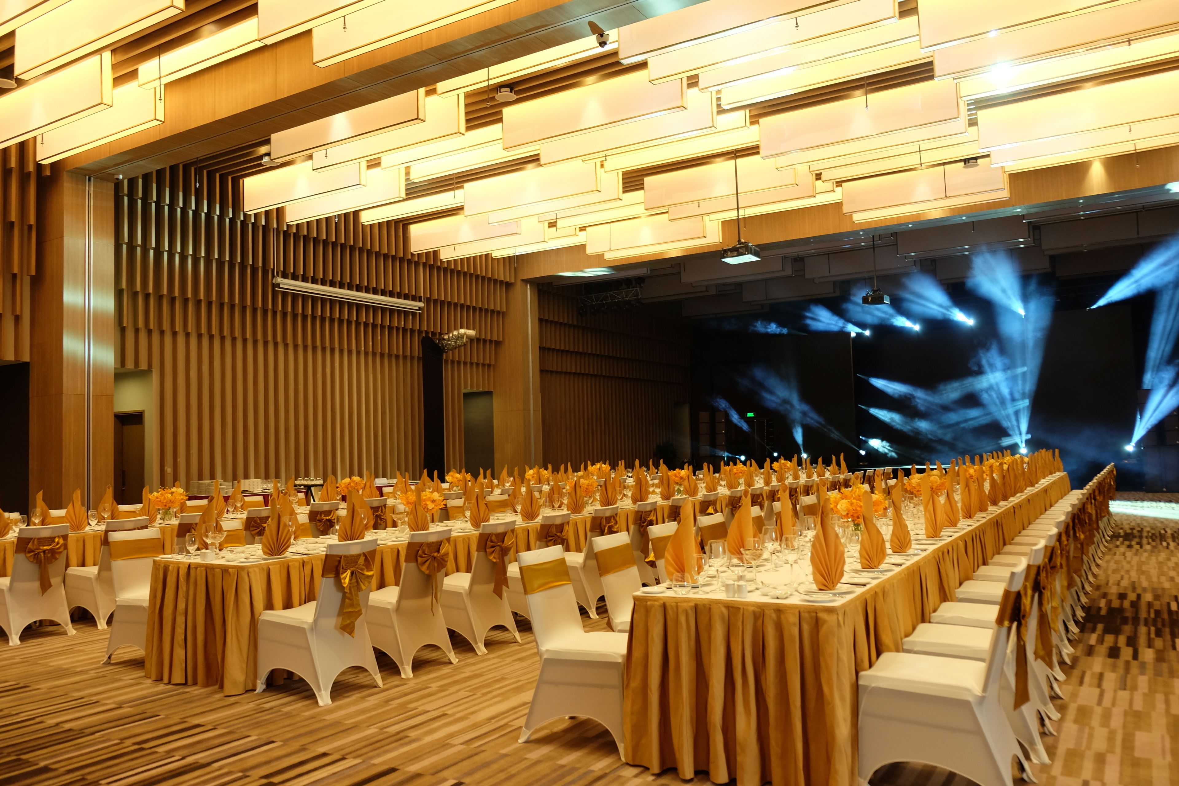 A banquet hall with rows of tables, white chairs, and golden accents.