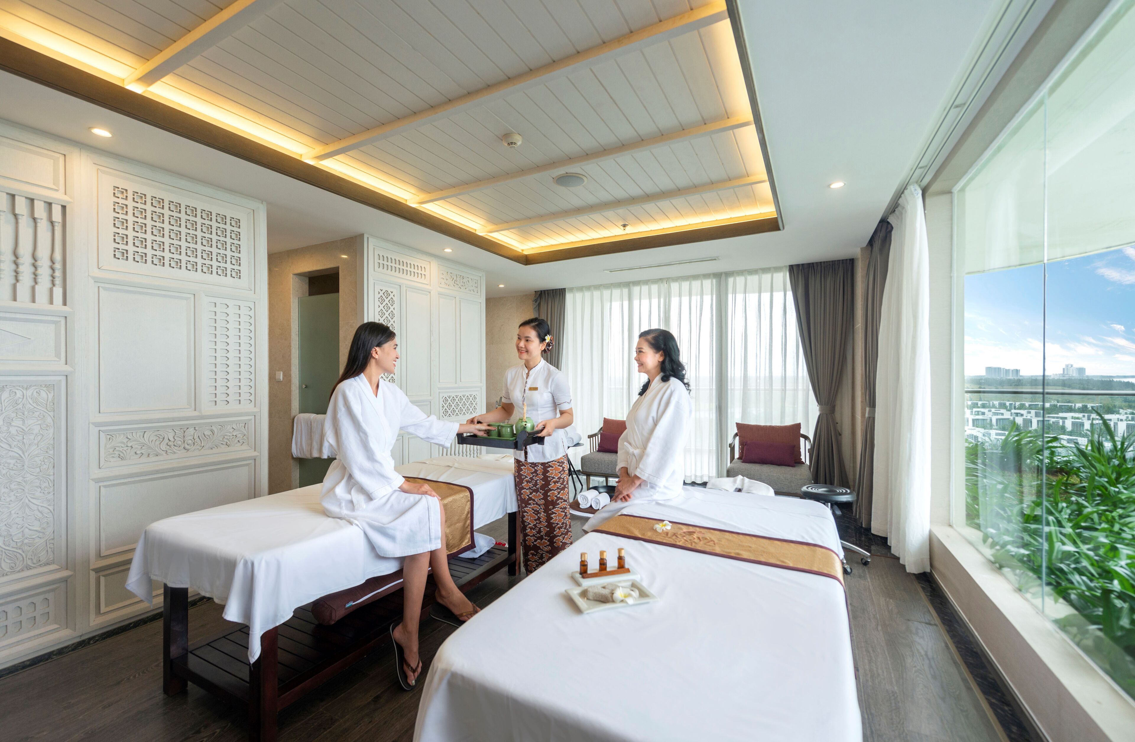 Et hotelværelse med en massageloungestol, seng, massageterapeut og en gæst, der modtager massage.
