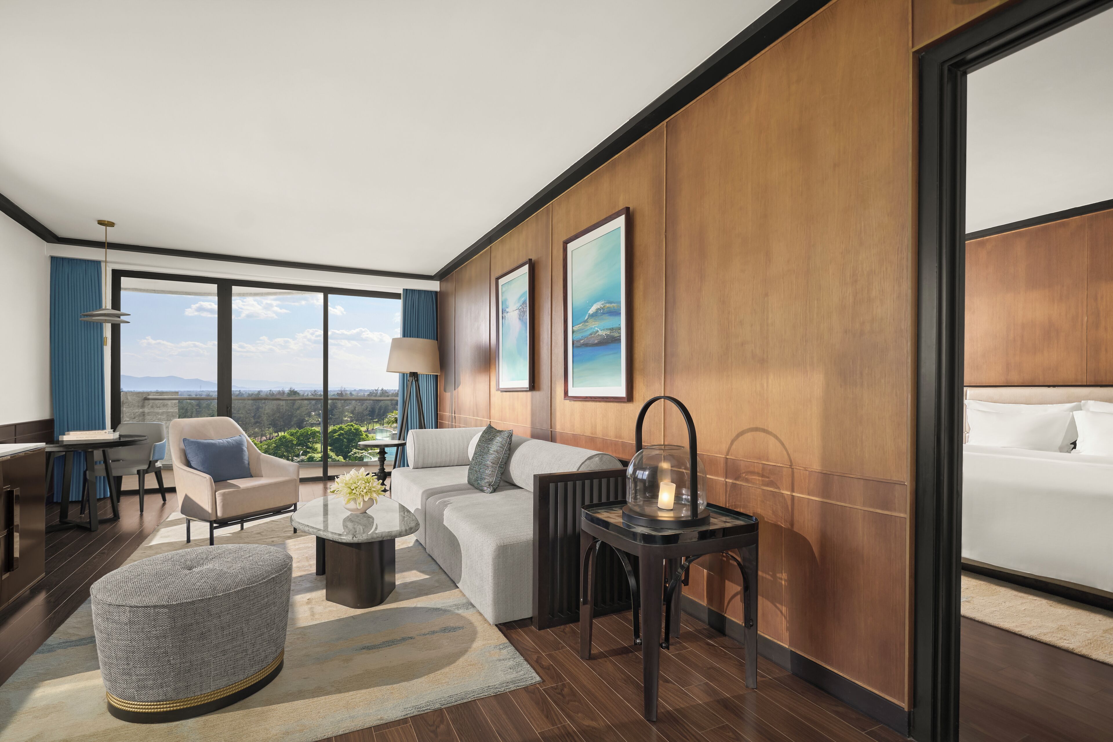 A modern hotel room with a large window, a sofa, a coffee table, and a lamp.