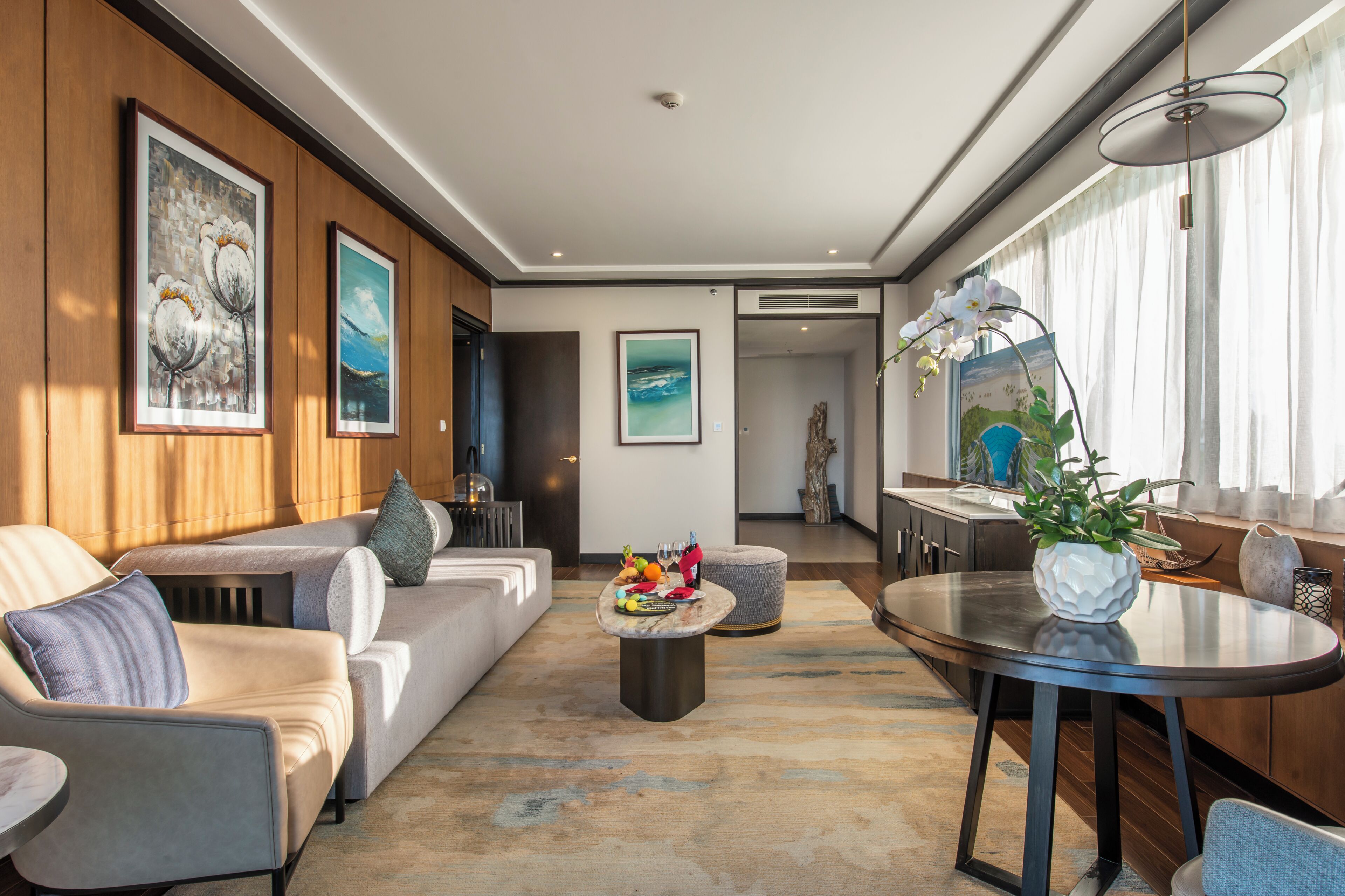 A modern living room with a sofa, a coffee table with fruits and glasses, and a dining area with a table and chairs.