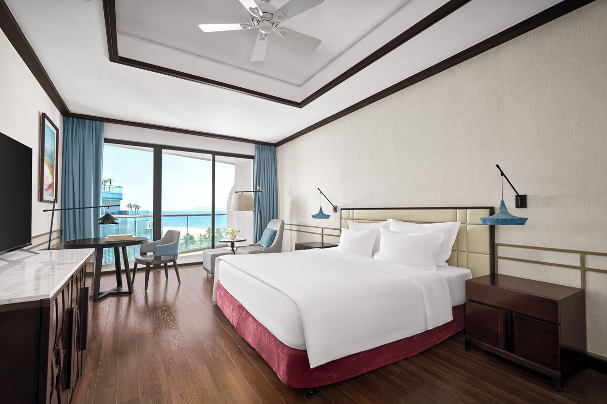 Een hotelkamer met een bed, bureau, stoel en uitzicht op de oceaan.
