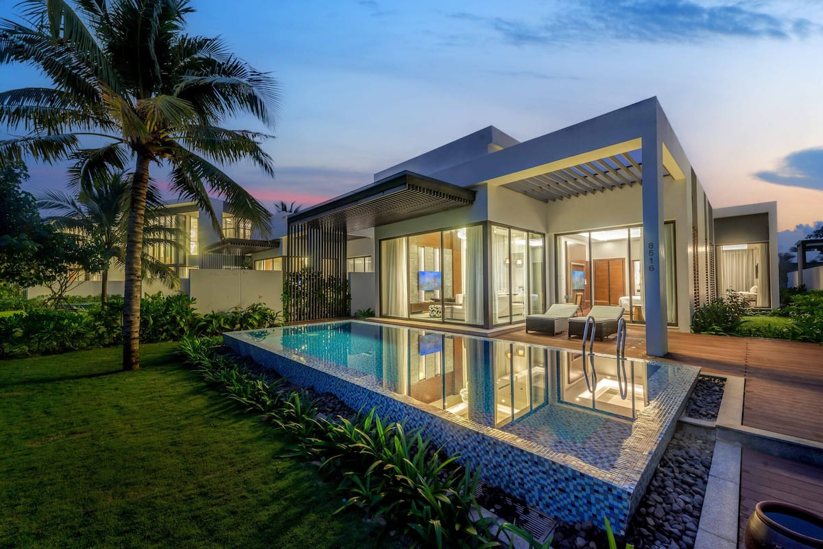 Une maison moderne dotée d’une piscine, de grandes fenêtres et d’un jardin bien entretenu.