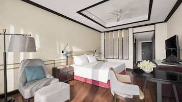 A hotel room with a bed, a desk, a chair, a nightstand, a lamp, and a ceiling fan.