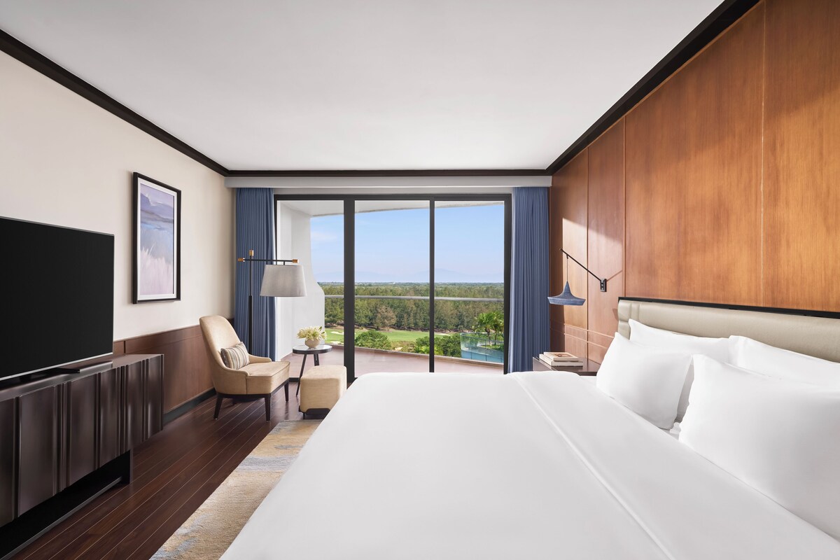 Een hotelkamer met een groot bed, een flatscreen televisie, een bureau, een stoel en uitzicht op het groen.