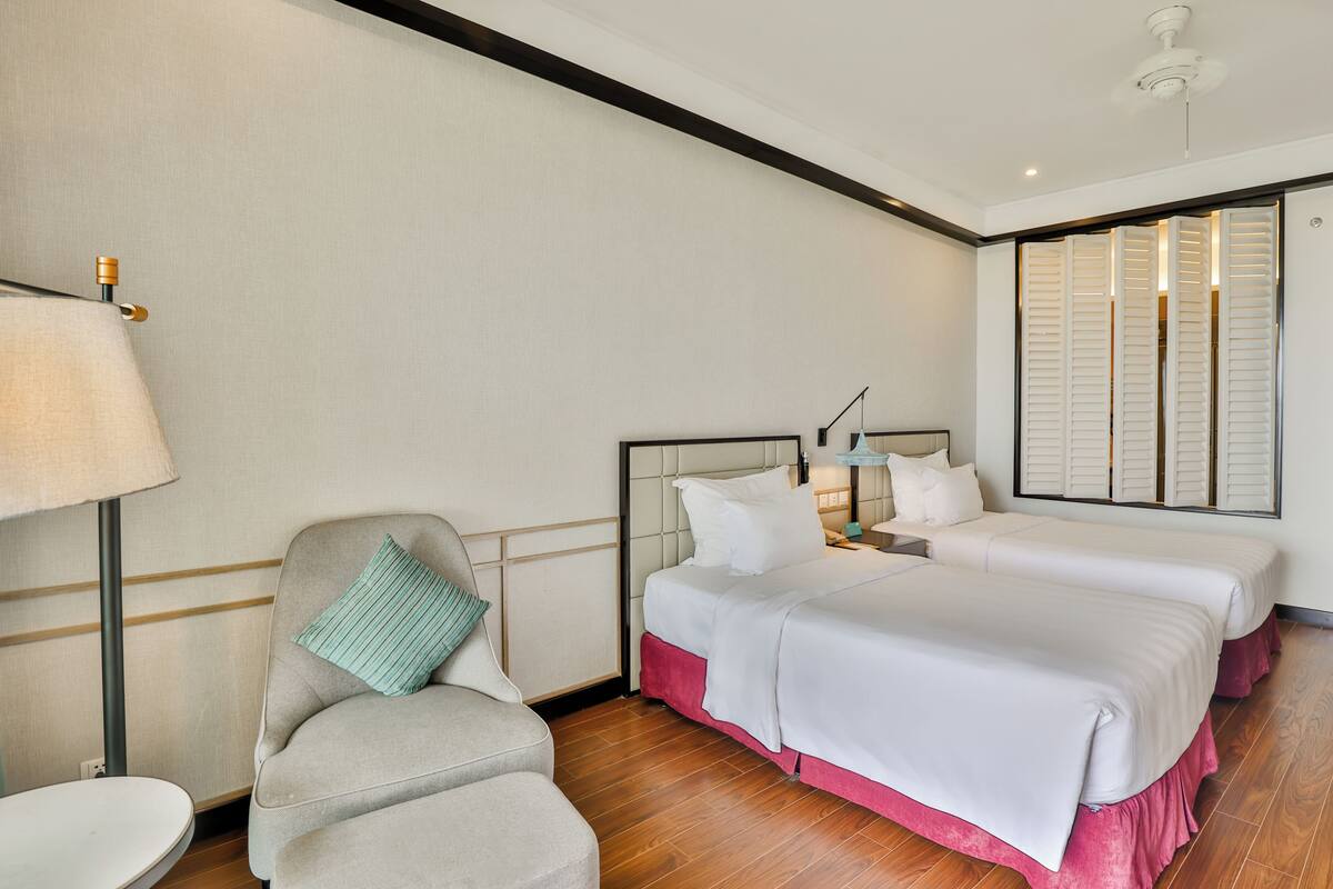 Une chambre d’hôtel avec deux lits, une chaise, une lampe et une fenêtre avec des volets.