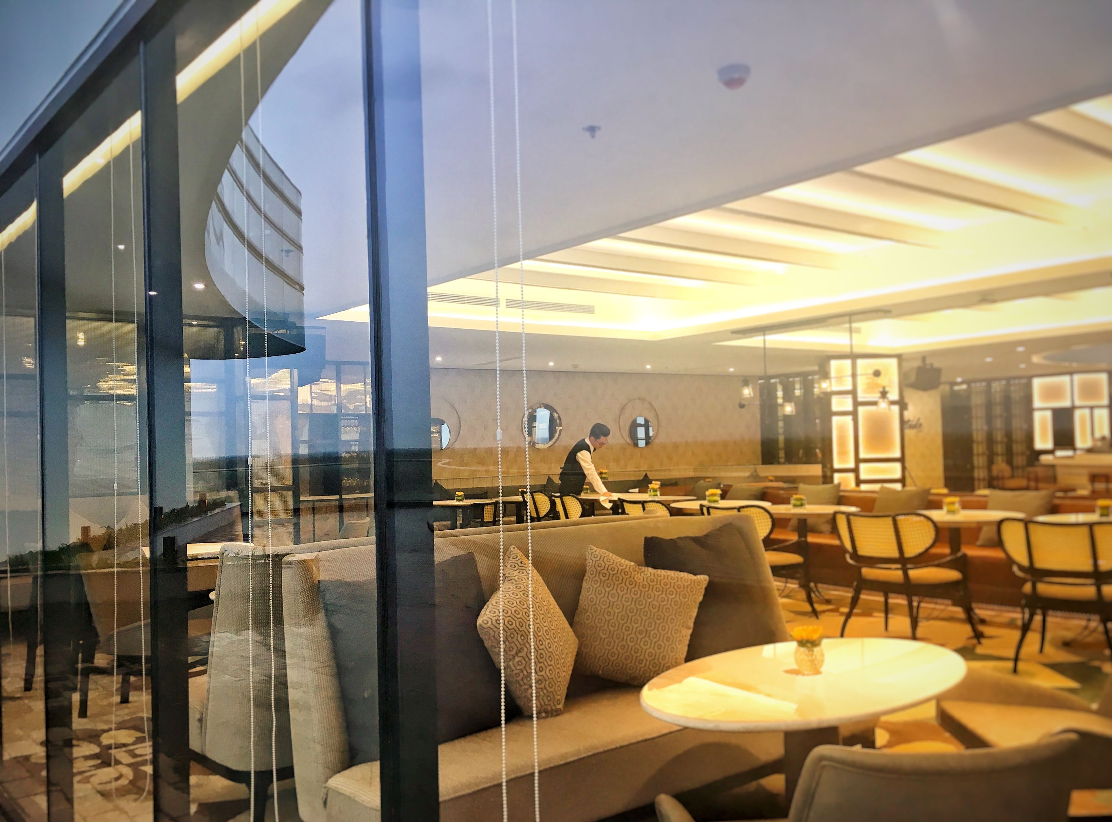 Un hall d’hôtel moderne avec une cloison en verre, des espaces de détente confortables et un intérieur bien éclairé.