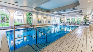 Une grande piscine intérieure à l’eau d’un bleu limpide, entourée d’un sol et de murs recouverts de carreaux blancs.