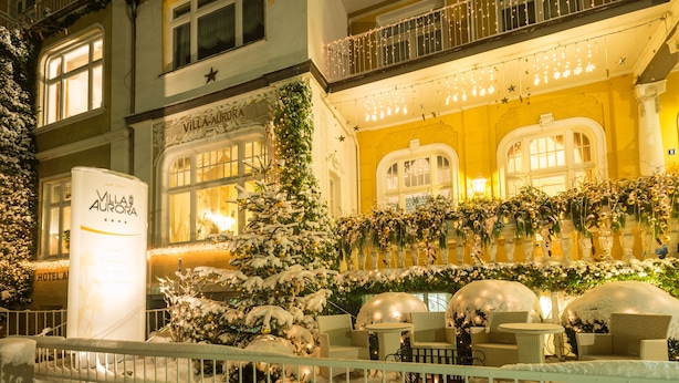 L’extérieur d’un hôtel, avec des plantes recouvertes de neige, des sièges en plein air et une lumière chaleureuse qui émane de l’intérieur.