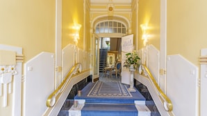 Un magnifique escalier avec un tapis bleu, des murs blancs et des éléments décoratifs dorés.