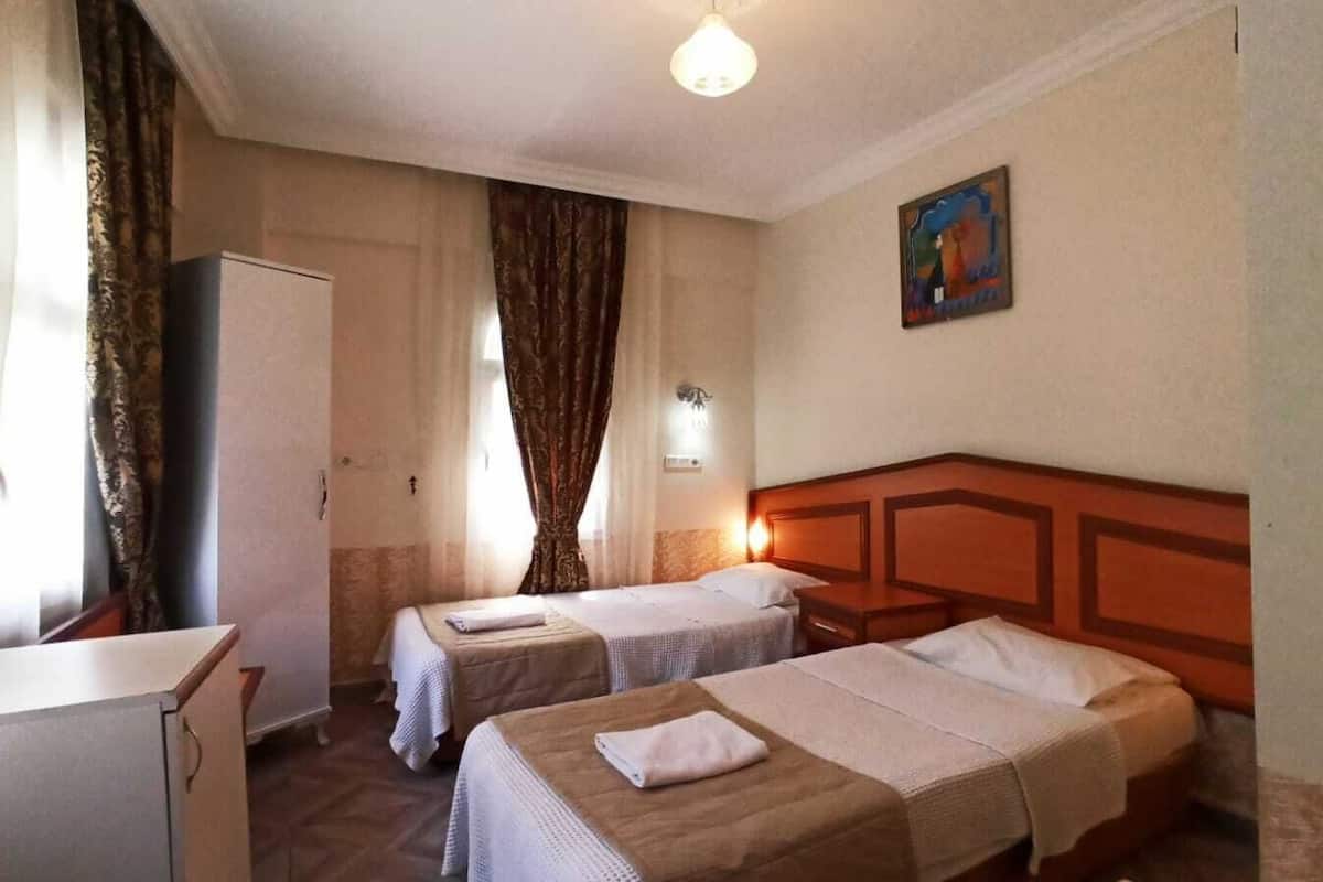 Een hotelkamer met twee enkele bedden, een houten hoofdbord, een bureau, een kledingkast en een schilderij aan de muur.