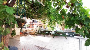 An outdoor seating area with tables and chairs, surrounded by greenery and a building in the background. - Ideal Pansiyon (Fethiye)