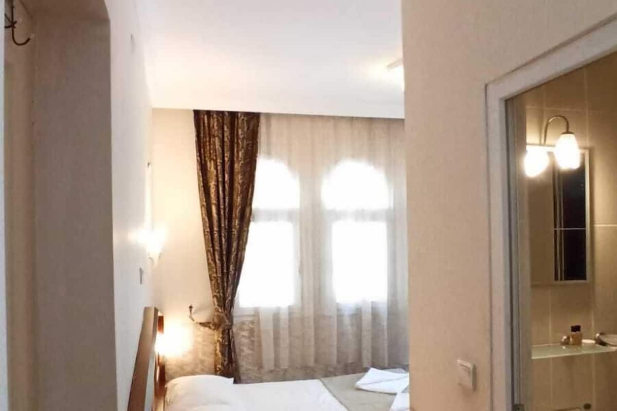 Een hotelkamer met twee bedden, een houten nachtkastje, een badkamer met een wastafel en spiegel, en een raam met gordijnen.