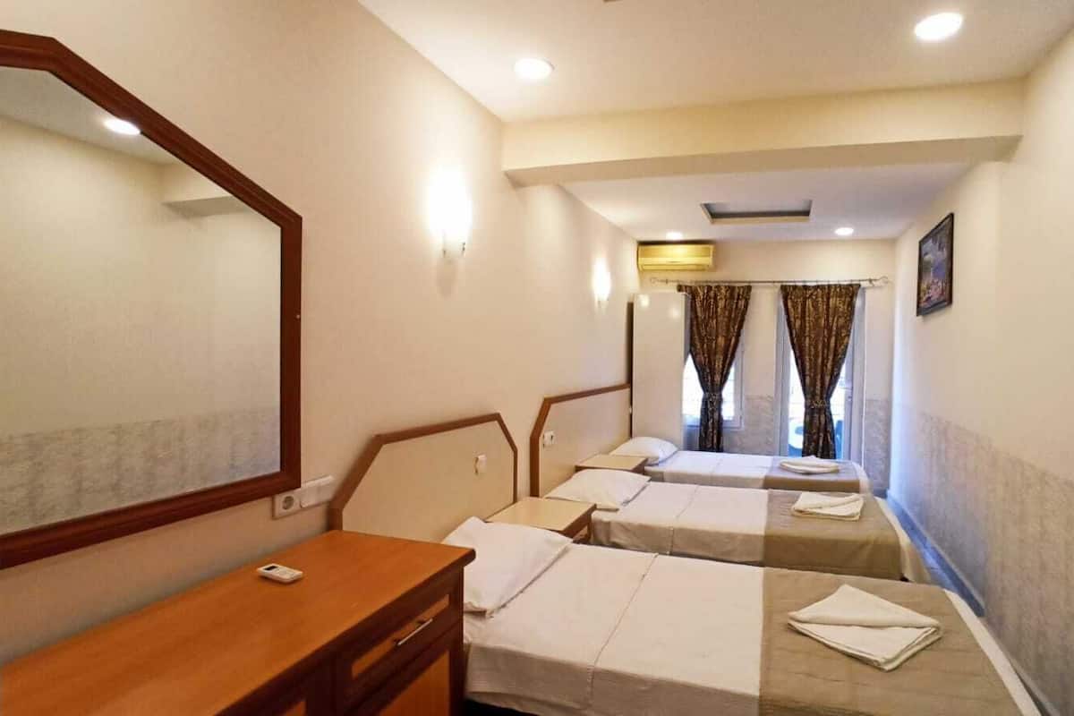 Een hotelkamer met drie eenpersoonsbedden, een houten bureau, een spiegel en een raam met gordijnen.