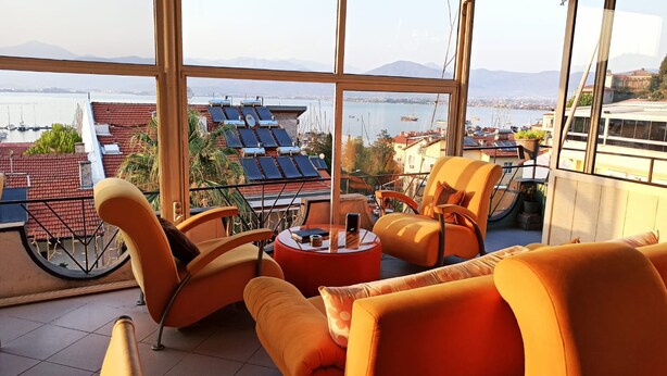 A balcony with orange chairs and a table, overlooking a marina with boats and solar panels on rooftops. - Ideal Pansiyon (Fethiye)