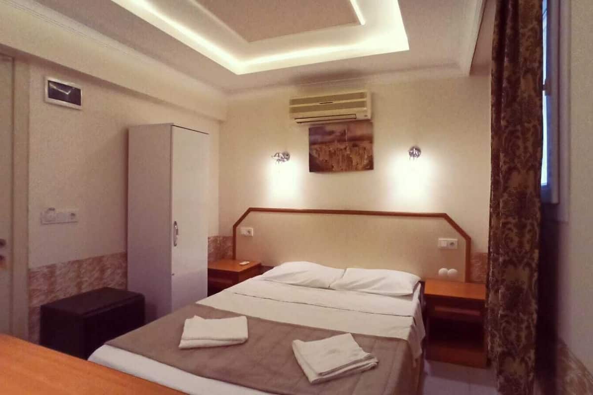 Een hotelkamer met een bed, nachtkastjes, een kledingkast en een schilderij aan de muur.