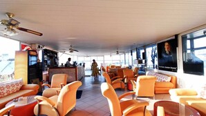 A spacious lounge area with orange chairs, a bar, and large windows offering a view. - Ideal Pansiyon (Fethiye)