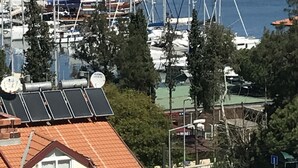 A marina with multiple sailboats docked, surrounded by trees and buildings, with a mountainous backdrop. - Ideal Pansiyon (Fethiye)