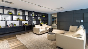 A modern living room with a sofa, ottoman, and a bookshelf filled with decorative items. - The William Suites (Melbourne)