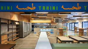 A modern restaurant interior with a long counter, seating area, and kitchen in the background. - The William Suites (Melbourne)