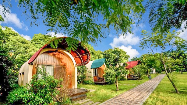 Un chalet rustique avec une porte en bois et un auvent rouge, entouré d’une végétation luxuriante et bordé d’un chemin pavé.