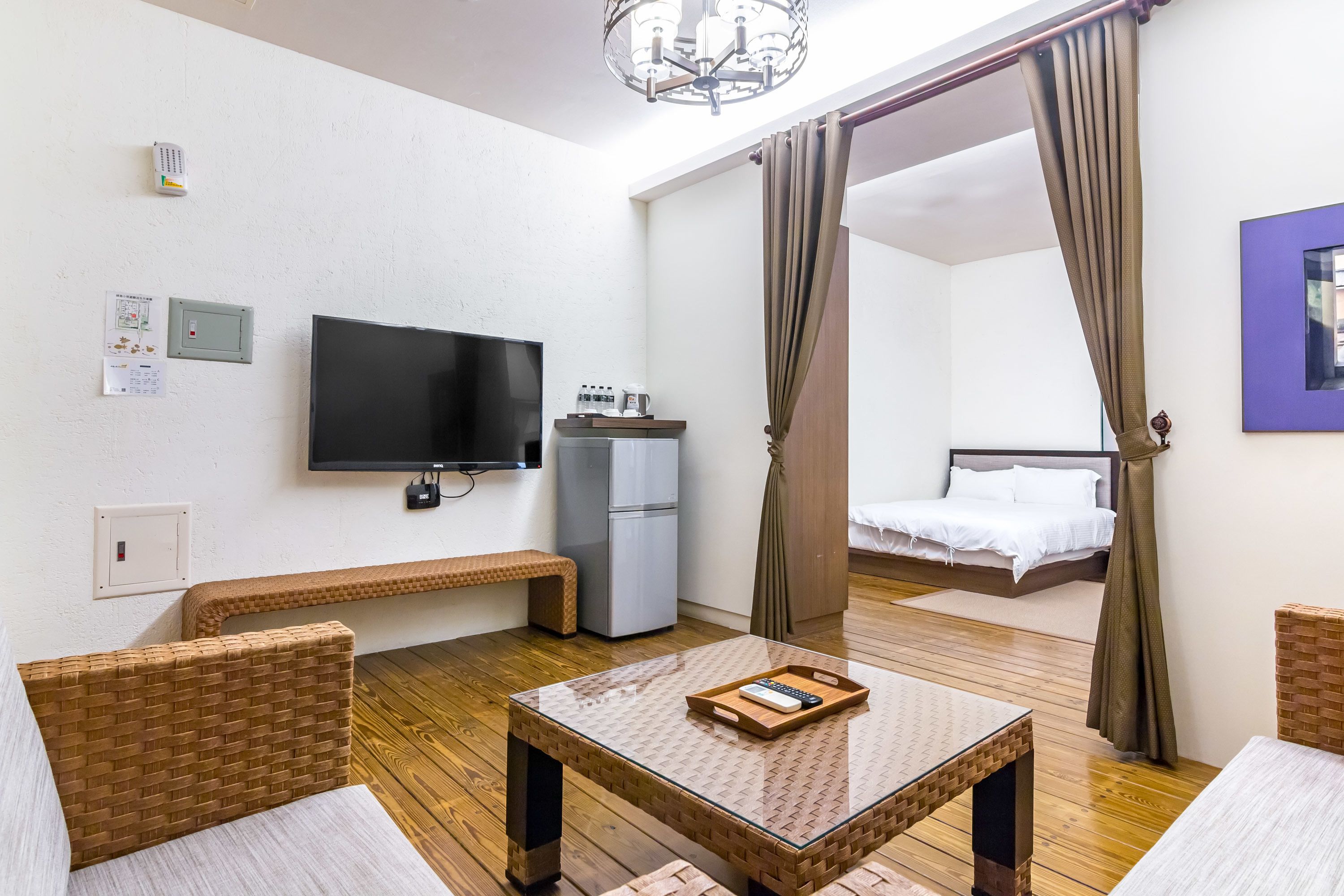 Ett hotellrum med en tv, en minibar, en säng med draperingar, möbler i rotting och ett trägolv.