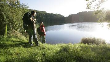 A serene lakeside scene with a person and a child standing by the water's edge, surrounded by lush greenery.