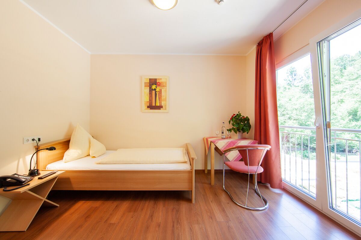 Une pièce de taille modeste, comprenant un lit, un bureau, une chaise et une fenêtre avec des rideaux.