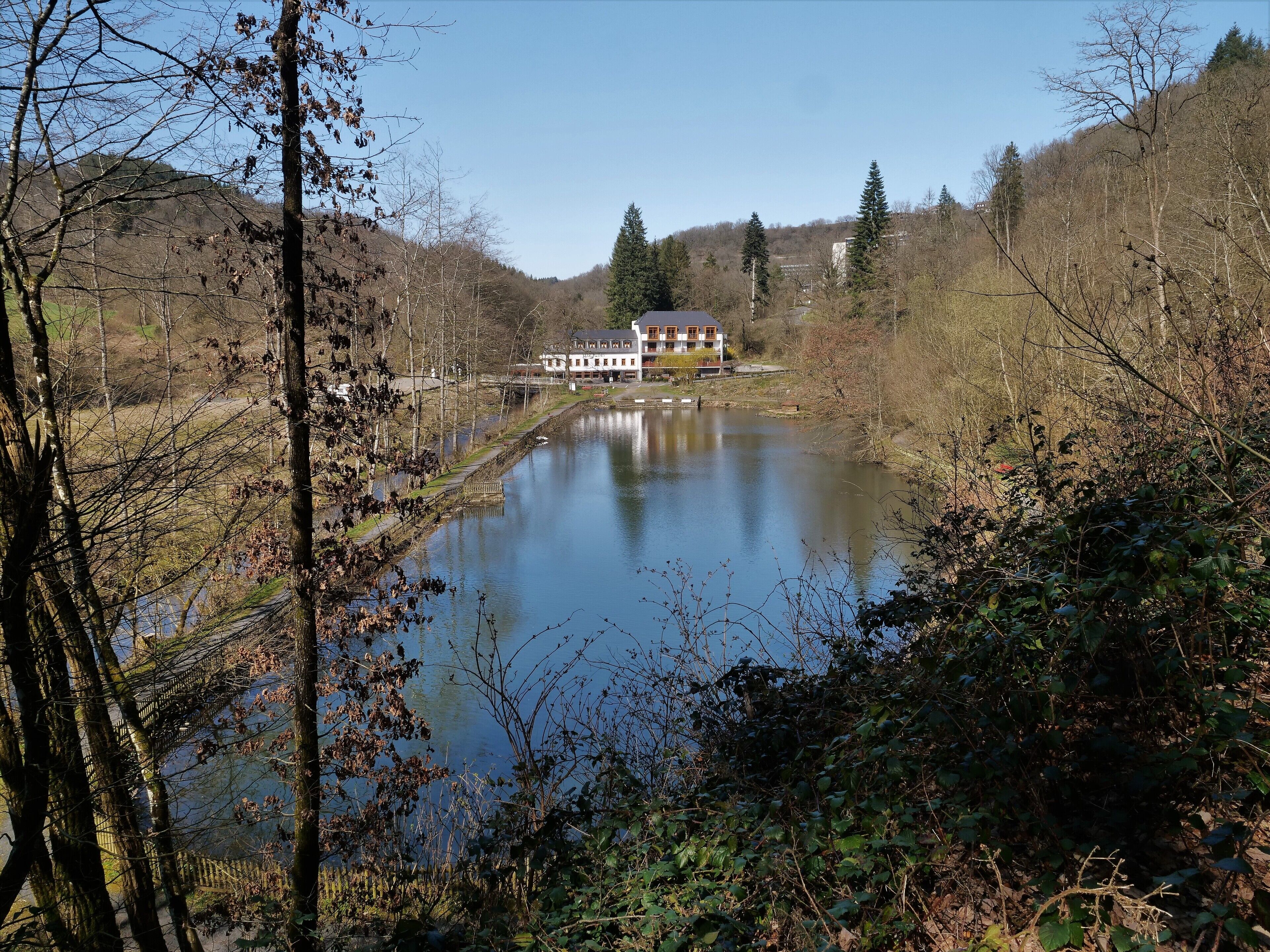 A riverside hotel with a long building, a bridge, and a forested hillside.