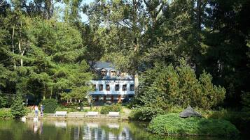 A lakeside hotel with a classic design, surrounded by dense forest and a calm lake.