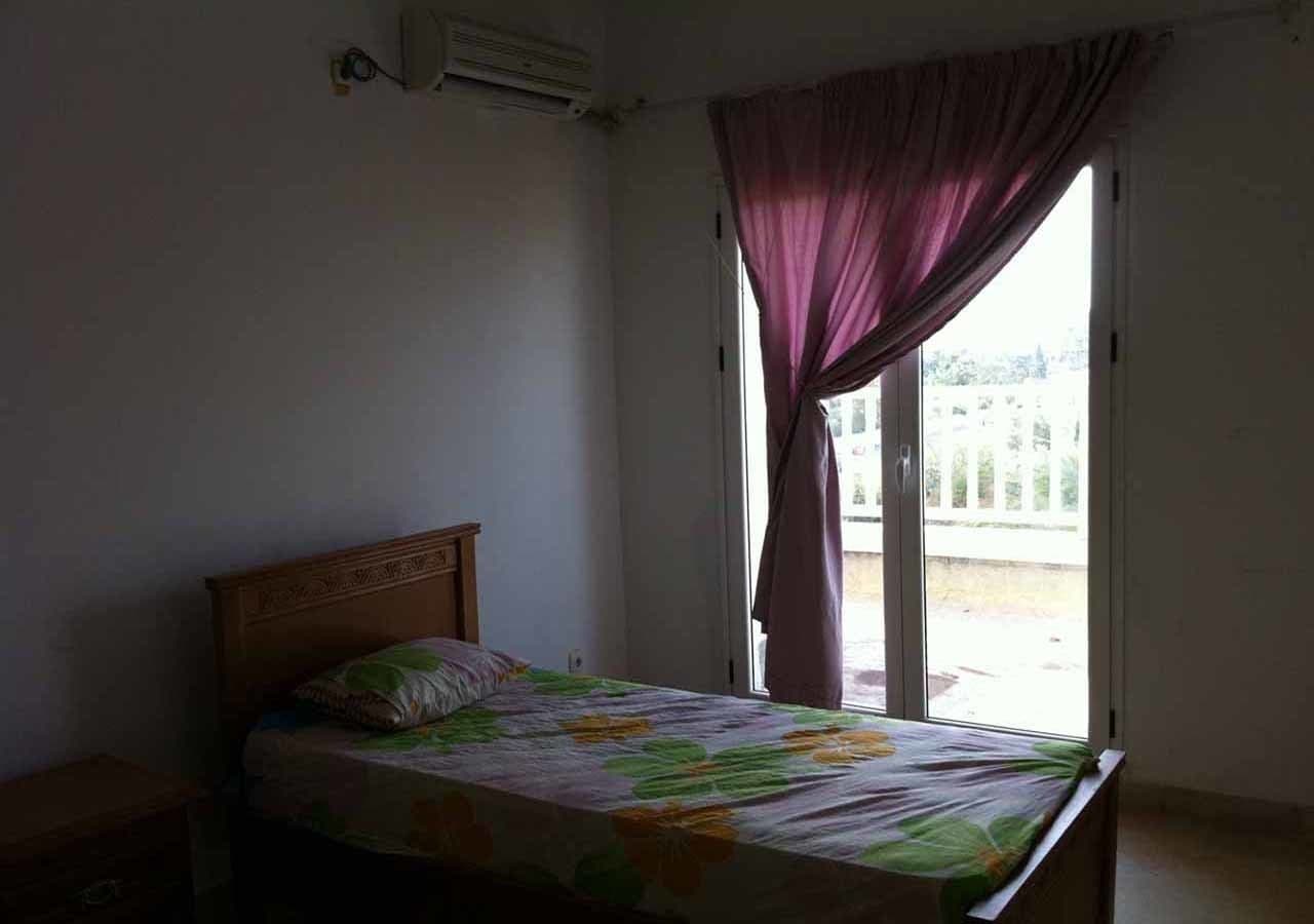 Una camera da letto con un letto, un comodino, una finestra con tende e vista all'esterno.