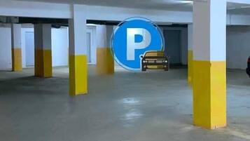 Un aparcamiento con pilares amarillos, un cartel azul grande con la letra 'P' y un coche a lo lejos.