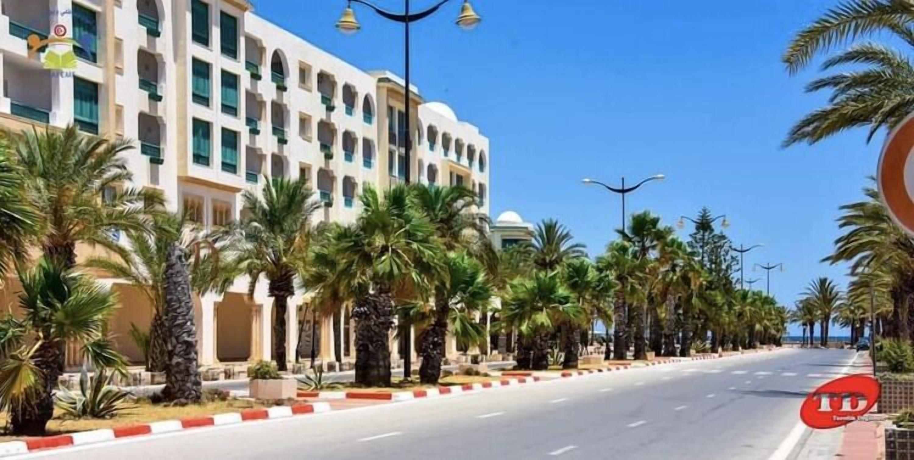 A hotel with a row of palm trees and a clear blue sky.