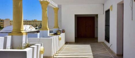 A corridor with white walls and yellow columns, leading to a door.