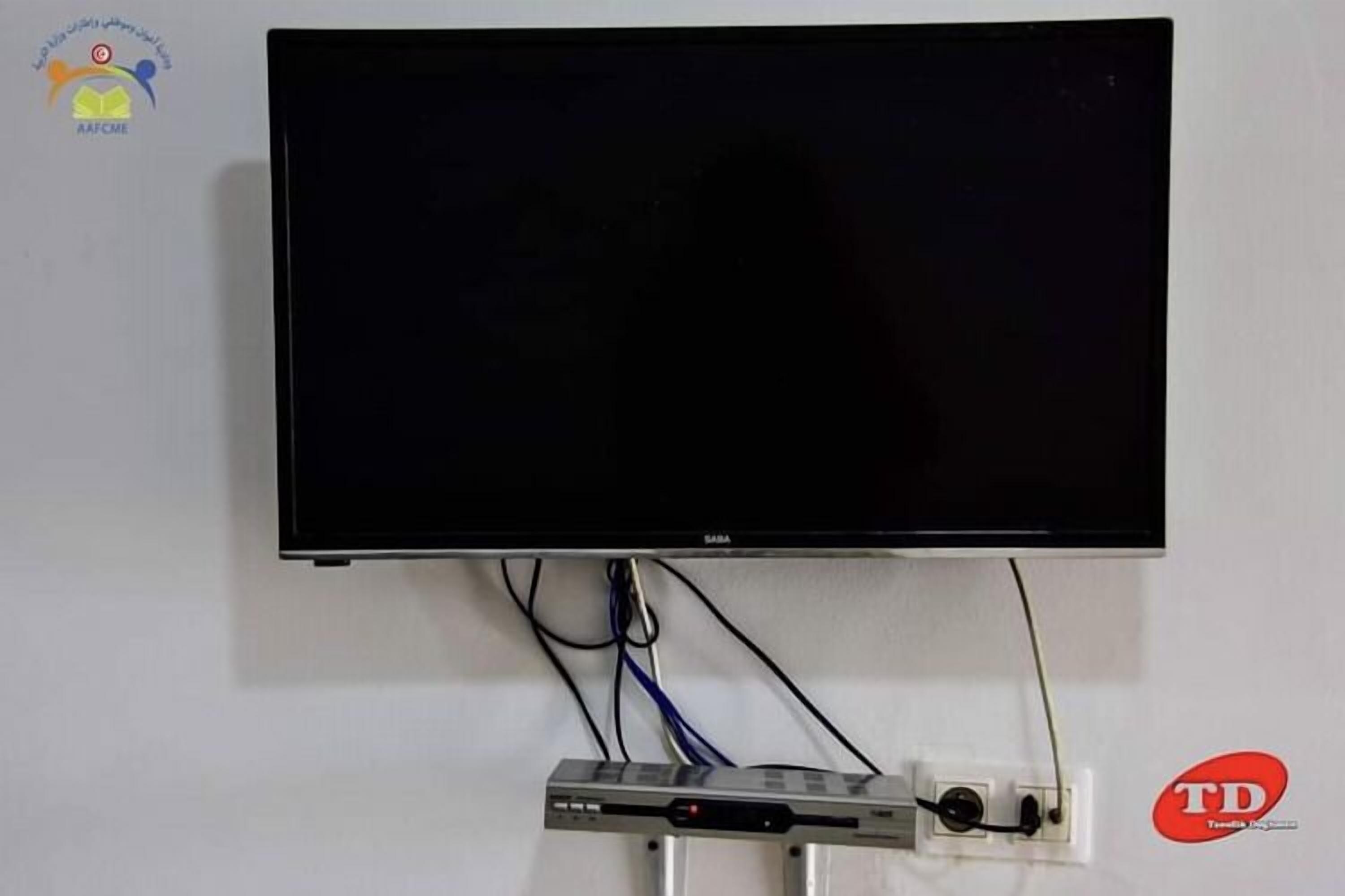 Televisor de pantalla plana montado en una pared blanca, con cables visibles y una regleta eléctrica debajo.