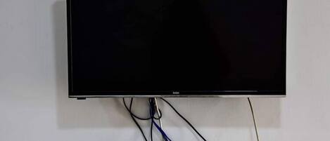 Televisor de pantalla plana montado en una pared blanca, con cables visibles y una regleta eléctrica debajo.