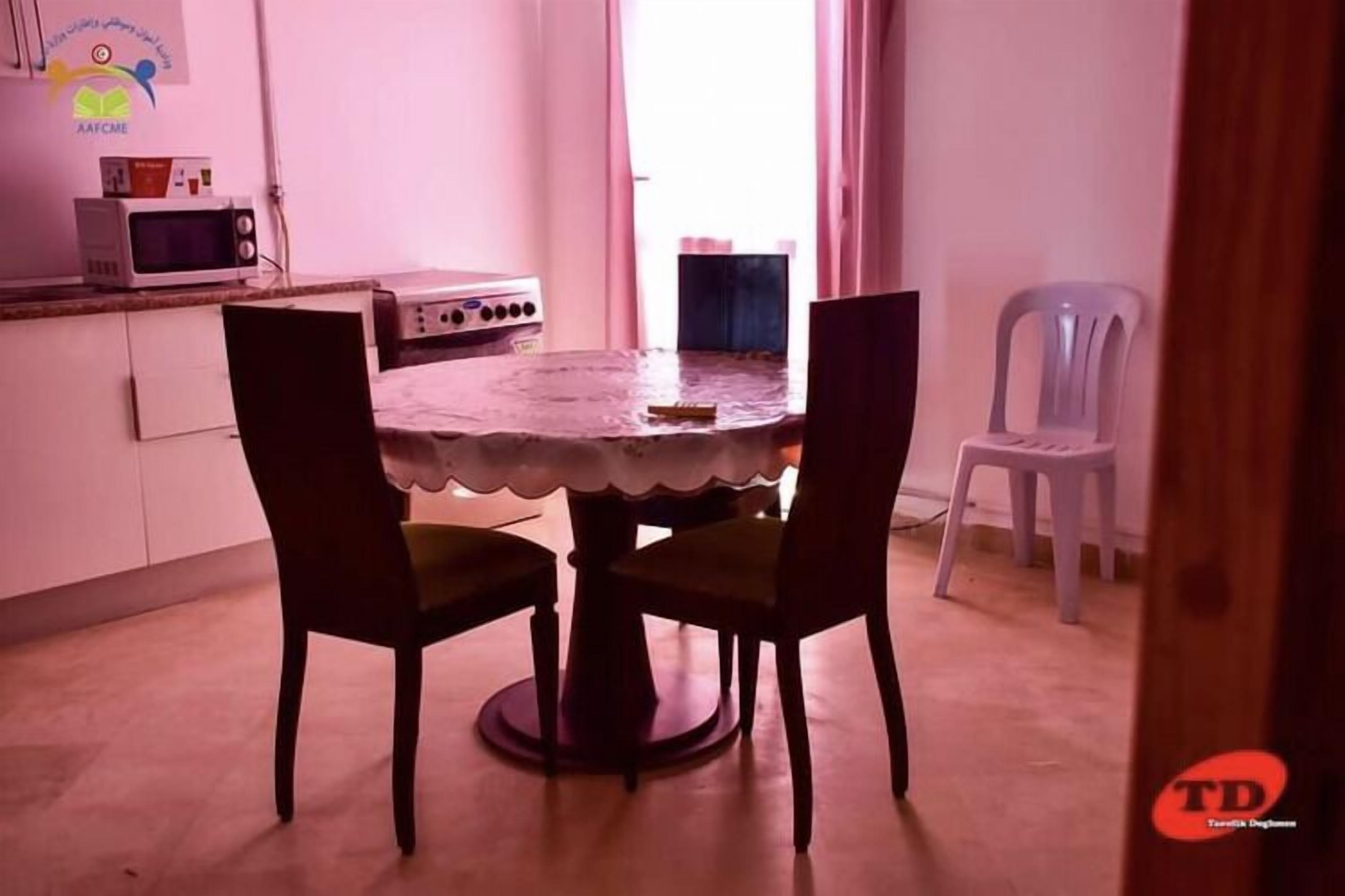 A dining area with a round table, two chairs, a microwave, a stove, and a window with curtains.