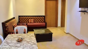 A living room with a sofa, a coffee table, and a TV mounted on the wall. - Residence Aladin (Hammamet)