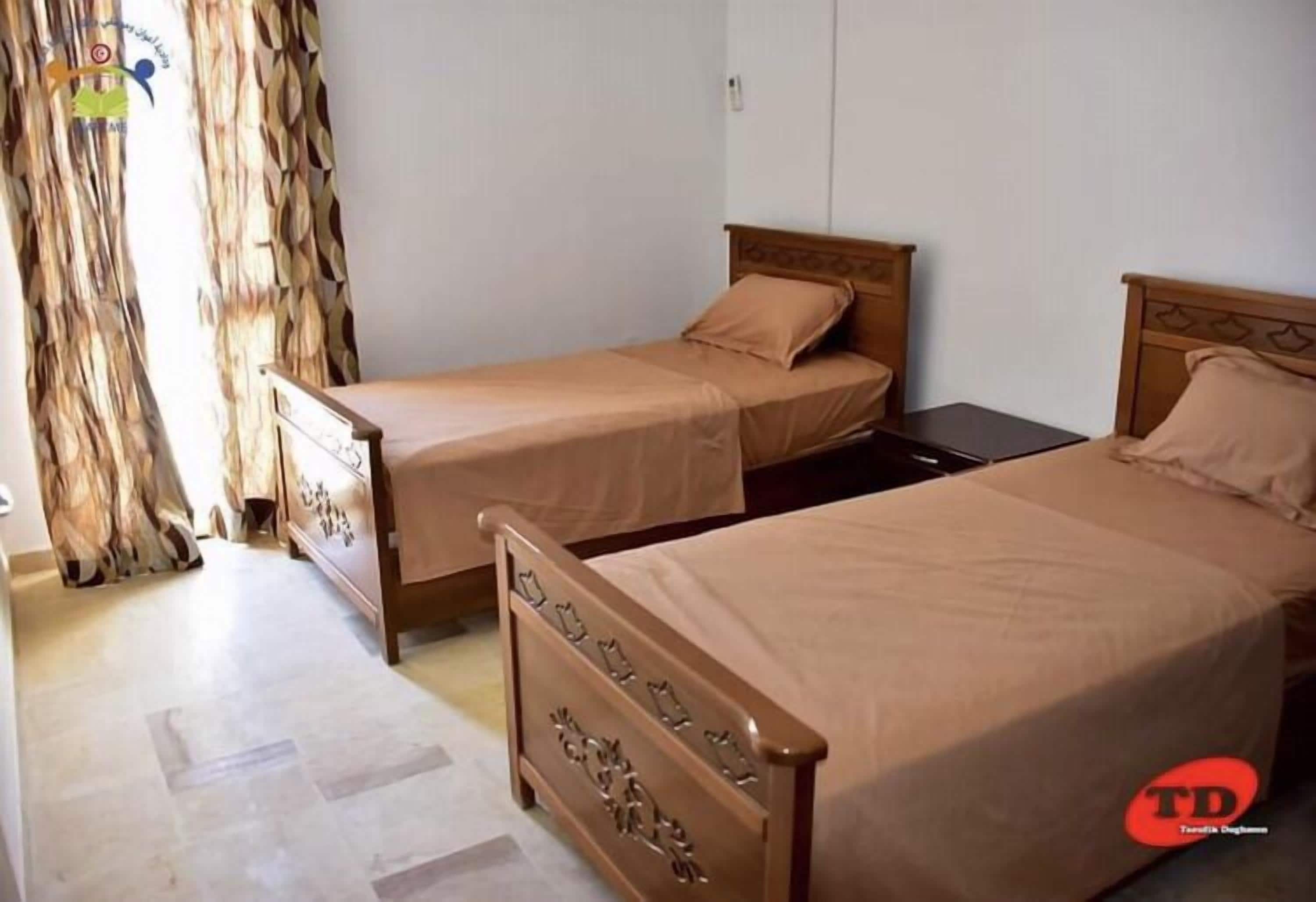 A room with two wooden beds, a small table, and a curtain.