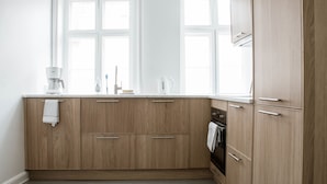 A modern kitchen with wooden cabinets, a white countertop, and a window above the sink. - 3 Bedroom Apartment in Latin Quarter (Copenhagen)