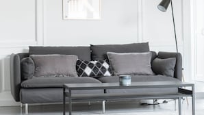 A modern living room with a grey sectional sofa, a small side table, and a floor lamp. - 3 Bedroom Apartment in Latin Quarter (Copenhagen)