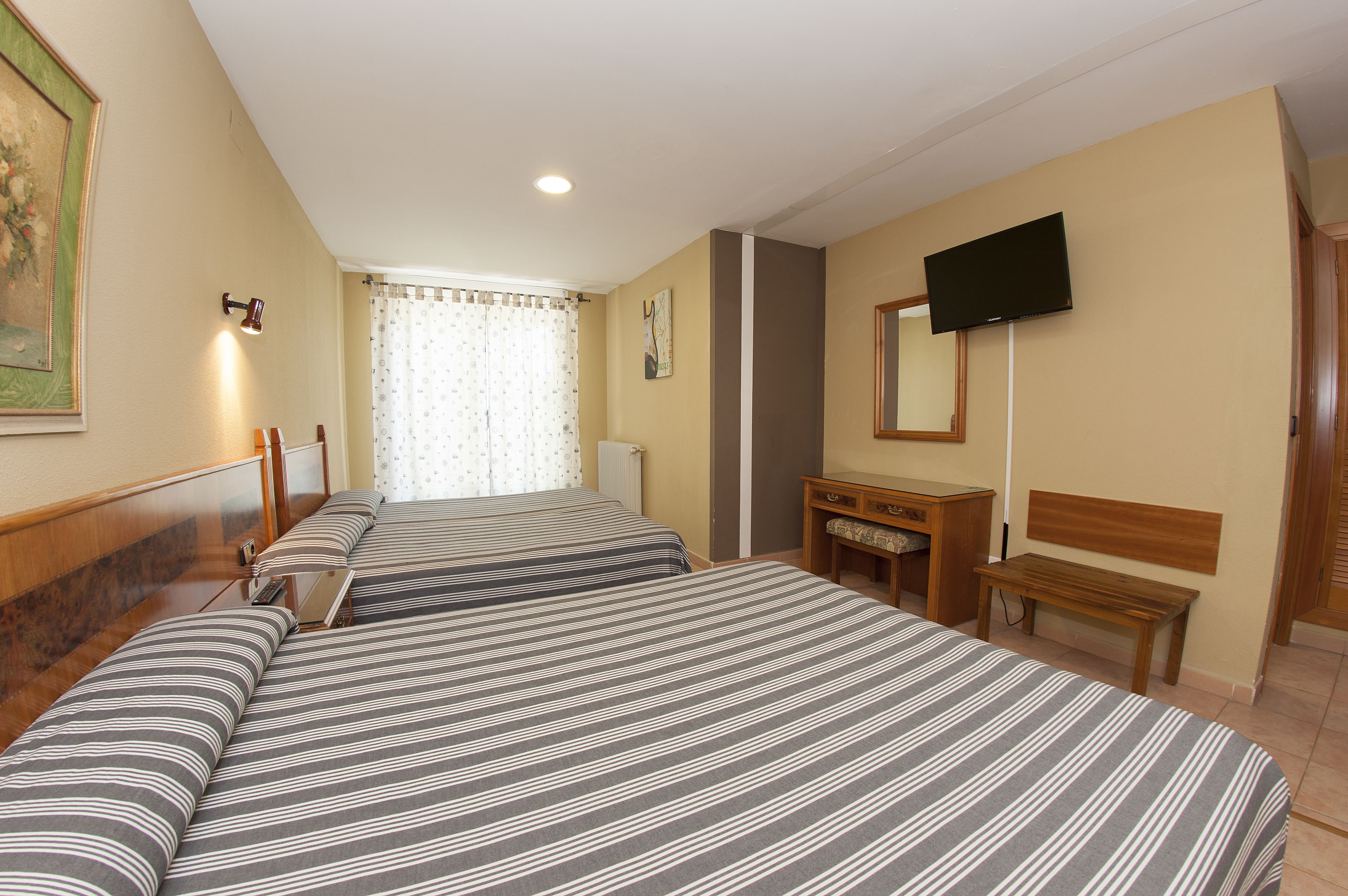 A hotel room with two beds, a desk, a chair, a television, and a mirror.