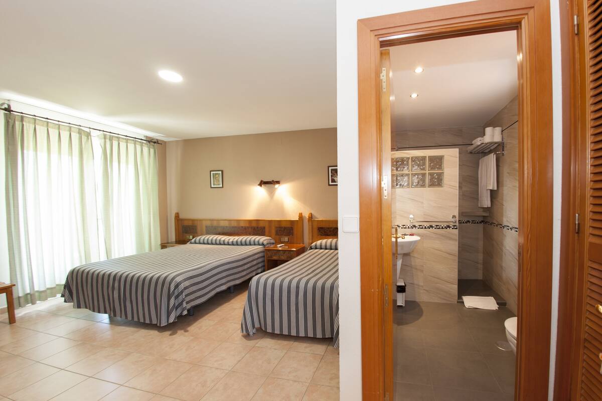 Une chambre d’hôtel avec deux lits, une salle de bain équipée d’un lavabo et d’un miroir, et une porte en bois.