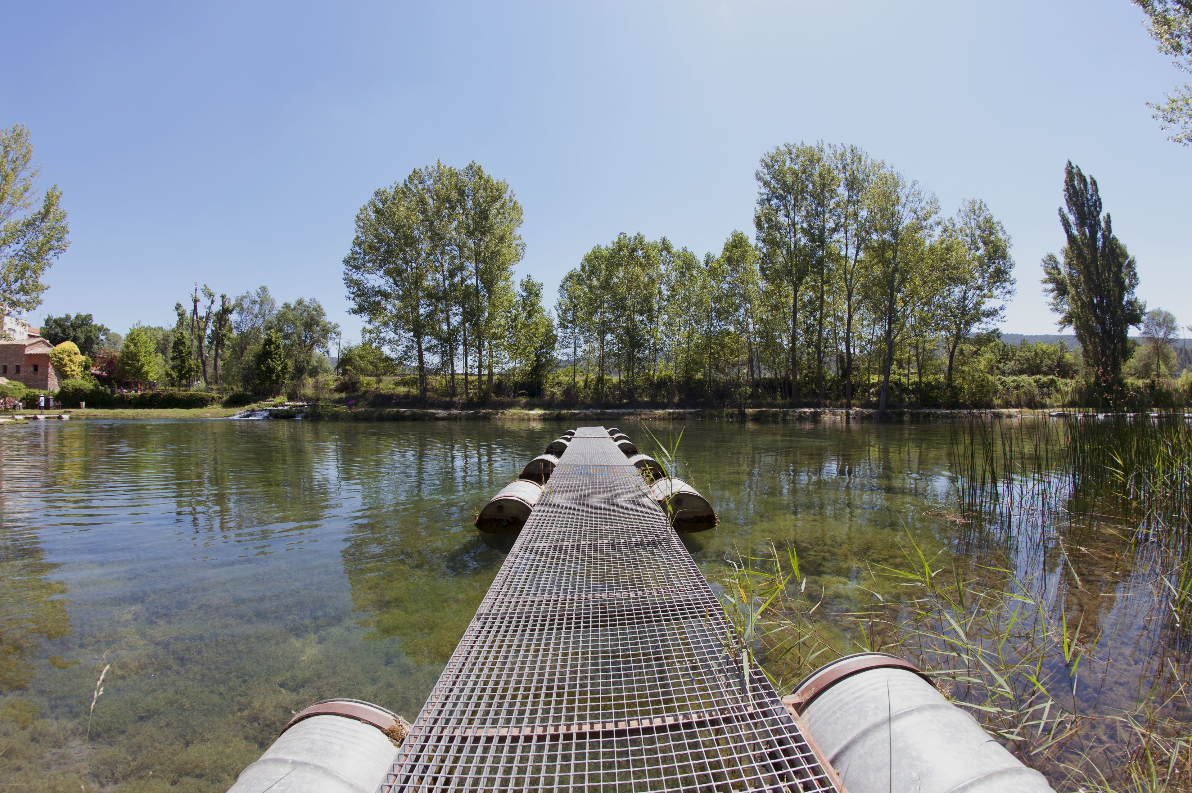 Un puente metálico sobre aguas tranquilas, flanqueado por árboles a ambos lados.