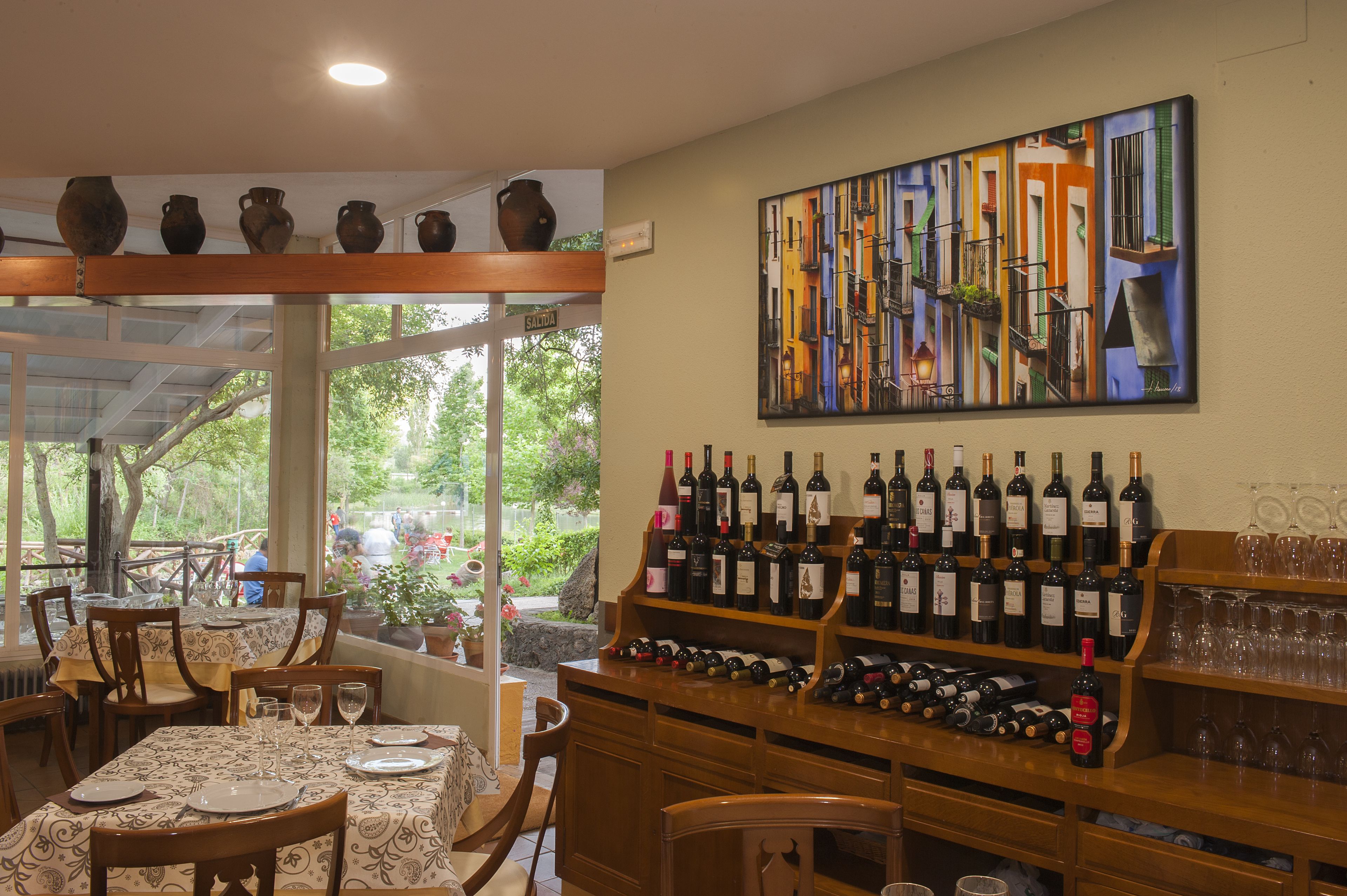 A restaurant with a wine display, dining tables, chairs, and a large window overlooking greenery.