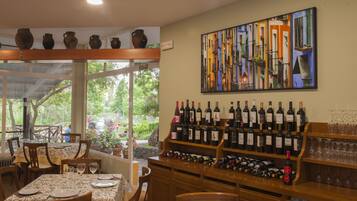 A restaurant with a wine display, dining tables, chairs, and a large window overlooking greenery.