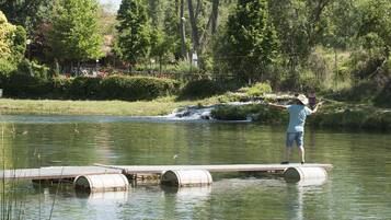 A person standing on a wooden platform over water, surrounded by greenery and trees.