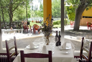 An outdoor dining area with tables set for two, chairs, and a vase with flowers. - Hotel Restaurante El Tablazo (Villalba de la Sierra)