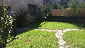 Un edificio rústico de piedra con jardín, que incluye un sendero de piedra, un farol y plantas con flores.